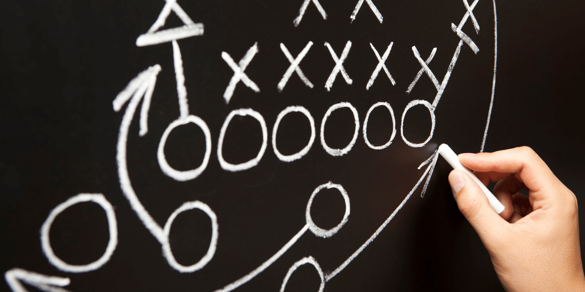 A football play being drawn on a blackboard in chalk. 