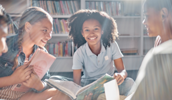 A group of girls sits in a library reading a book.