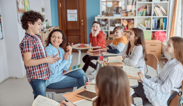 A boy stands in front of a teacher and group of students during a YMCA academic program. 