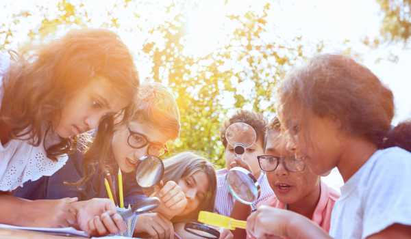 Summer youth program participants gather around with magnifying glasses for an engaging activity. 