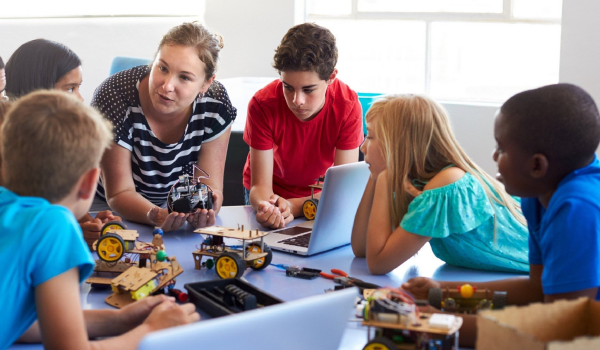 An afterschool program teacher huddlles at a table with a group of kids.