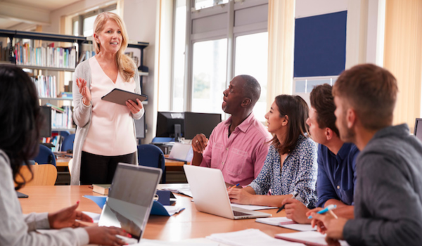 A youth program manager stands in front of a group of her program leaders at a staff meeting.
