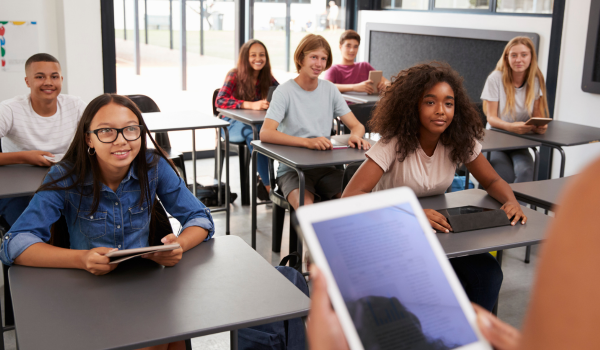 Teacher digitally accessing curriculum, assisting two children in their learning process.