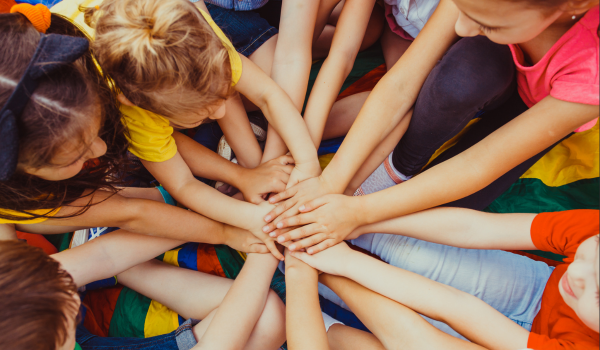 A group of children gather and put their hands in a circle at a summer youth program.