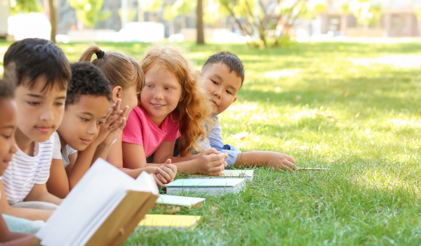 A group of children sit outside reading during a summer learning program.